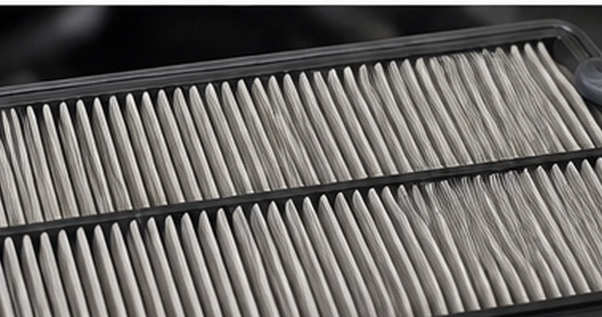 Technician holding a rectangular pleated engine air filter in front of an open engine bay